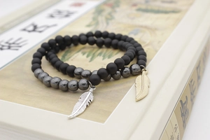 Detail of matte black and hematite beaded bracelets with feather charms on a book