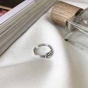 Detail view of S925 sterling silver knotted ring on white fabric with lifestyle props