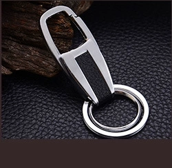 Detail of silver metal keychain with black leather inlay on premium dark wood background