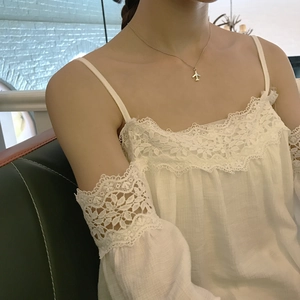 Detailed view of a silver airplane pendant necklace styled on a white lace top