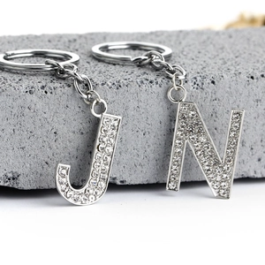 Macro detail of silver alloy alphabet J and N keychains with sparkling rhinestones on stone