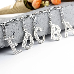 Macro detail of silver alphabet keychains with crystal rhinestones on a stone surface