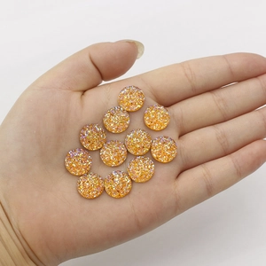 Hand holding 12mm round sparkling orange resin cabochons for DIY jewelry making