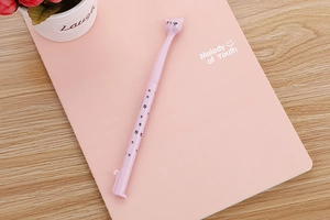 Pink cartoon cat gel pen with paw prints on wood desk near pink notebook