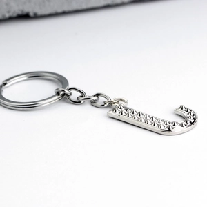 Detailed macro view of silver letter J keychain with metallic rivet textured surface