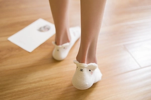 Close-up of white cotton socks with cute cartoon bear ears worn on wooden floor