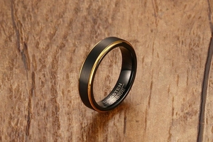 Detail of 5mm black matte tungsten carbide ring with gold center line on wood surface