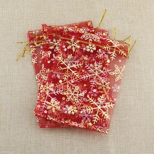 Detail of three red organza gift bags with gold snowflake prints on beige linen