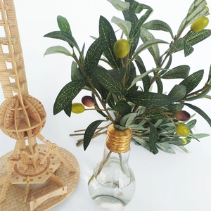 Detailed view of artificial olive branches with green and purple fruits in a glass vase