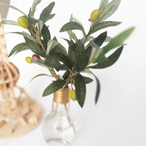 Artificial olive branch with green leaves and fruits in a light bulb glass vase