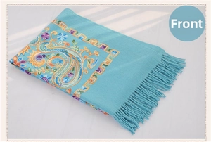 Detailed close-up of turquoise wool shawl with colorful paisley embroidery and fine tassels
