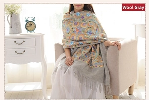 Detailed view of paisley embroidery and fringe tassels on a gray wool shawl