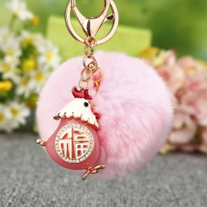 Gros plan du porte-clés en fourrure rose avec pendentif coq en strass et signe de chance