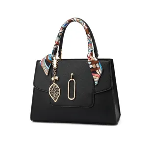 Detail of black leather handbag with silk scarf wrap and golden leaf pendant charm