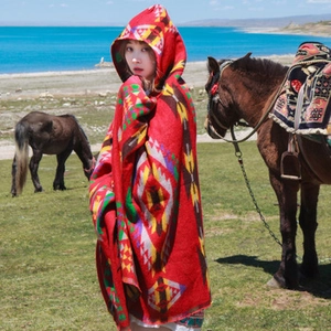 Close-up of red hooded poncho with ethnic geometric patterns and tassels in nature