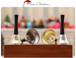 Detail of gold and silver Christmas hand bells with black handles on a wooden table