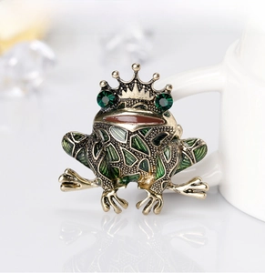 Macro shot of gold-plated frog king brooch with green enamel and crystal eyes