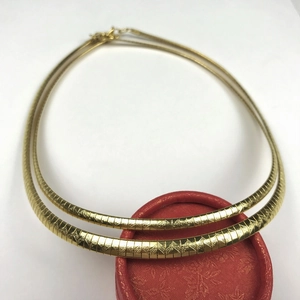 Detail of double-layer gold necklace with triangular geometric textures on flat snake chains
