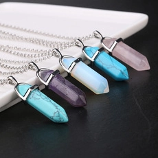 Close-up of hexagonal crystal point pendants in various colors on a white ceramic plate