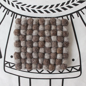 Detailed top view of a checkerboard square felt coaster with grey and brown wool balls