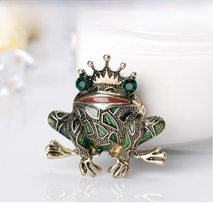 Macro shot of crown frog brooch with green enamel details and sparkling green gemstones
