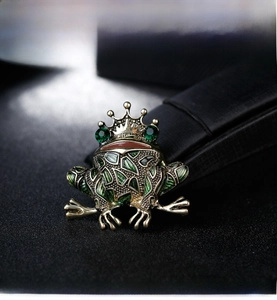 Macro view of vintage golden frog king brooch with green enamel and gemstone eyes