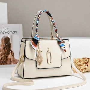 Minimalist beige crossbody bag with silk scarf and gold leaf charm on fashion magazine