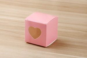 Détail d'une boîte à bonbons en papier kraft rose avec fenêtre cœur sur bois texturé