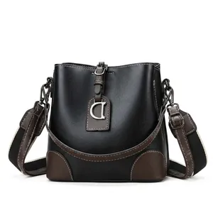 Détail du sac seau en cuir noir et marron avec pendentif D et bandoulière rayée