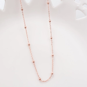 Macro detail of rose gold satellite chain necklace with beads on white ceramic background