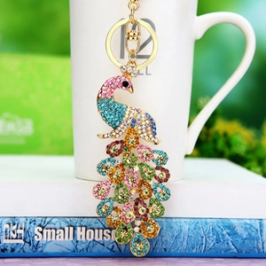 Close-up of a colorful rhinestone-studded peacock keychain hanging near a white ceramic cup