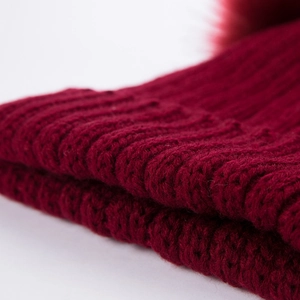 Dettaglio ravvicinato della trama a coste rosso scuro e del pompon di pelliccia sul cappello