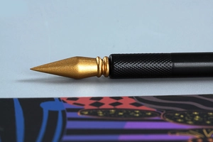 Macro shot of dual-purpose scraping pen with gold metal tip and black knurled handle