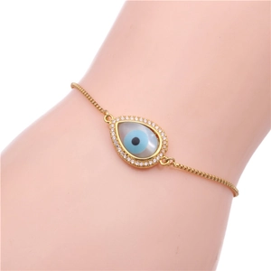Detail of gold evil eye bracelet with clear zircons and blue shell on female wrist