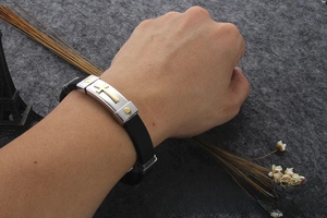 Detail of men's black silicone bracelet with stainless steel gold cross on the wrist