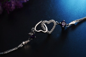 Macro shot of interlocking silver hearts bracelet featuring purple gems and white crystals
