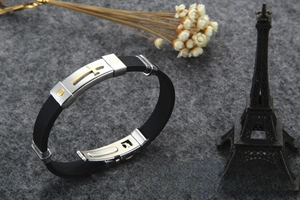 Detail of black silicone bracelet with stainless steel gold cross and rivet accent