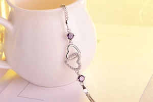 Detailed shot of silver heart bracelet with purple stones on a white ceramic cup