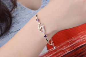 Detailed shot of interlocking silver hearts bracelet with purple crystals on a wrist