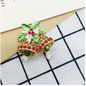 Detail of Christmas bell brooch with green holly leaves and red rhinestones on gold alloy