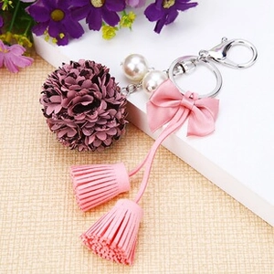 Close-up of floral keychain with purple fabric pompom, pearls, and pink ribbon bow