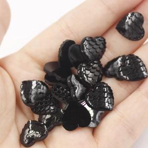 Macro shot of 12mm black heart-shaped resin charms with fish scale texture on palm