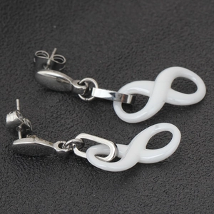 Detailed close-up of white ceramic infinity earrings with polished silver metal finish