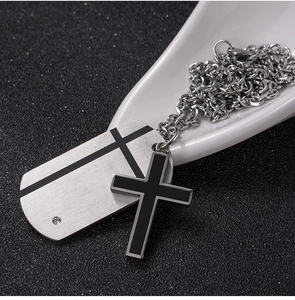 Close-up of brushed silver dog tag and black cross pendant necklace with small crystal