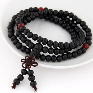 Classic black prayer beads with red accents and a brown Chinese knot tassel in a ceramic tray