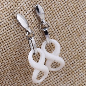 White ceramic and silver stainless steel infinity figure-eight drop earrings on linen