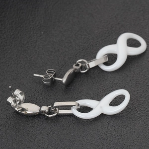 Macro shot of 40mm white ceramic infinity charm earrings on black textured surface