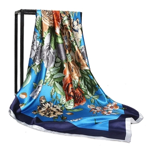 Blue silk-like 90cm square scarf featuring elegant floral patterns on a black display stand