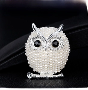 Macro shot of owl brooch with white pearls and black gemstone eyes on dark leather