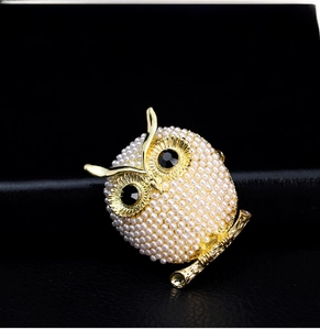 Close-up of golden owl brooch with white imitation pearls and black gemstone eyes